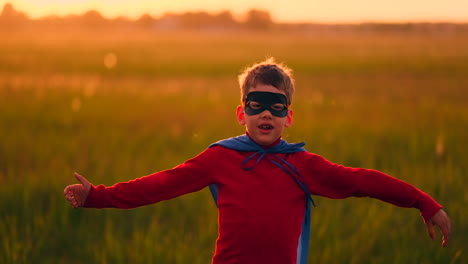 Un-Niño-Con-Traje-Y-Una-Máscara-De-Superhéroe-Corre-Por-El-Campo-Al-Atardecer-Sobre-El-Césped-Soñando-E-Imaginándose-A-Sí-Mismo-Como-Un-Héroe-Y-Un-Ganador.-Familia-Divertida-Y-Feliz